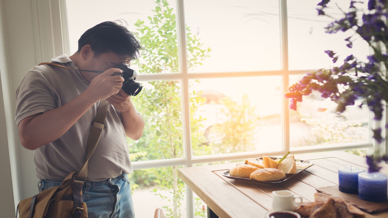 Photographer taking food photo near window in cafe.